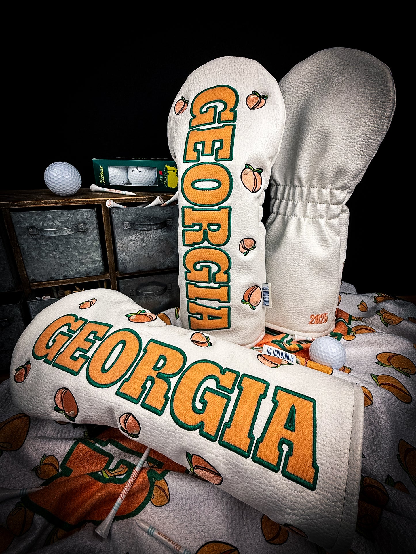 A golf club headcover featuring a pattern with the text 'Georgia' and images of peaches, displayed in a pro shop.