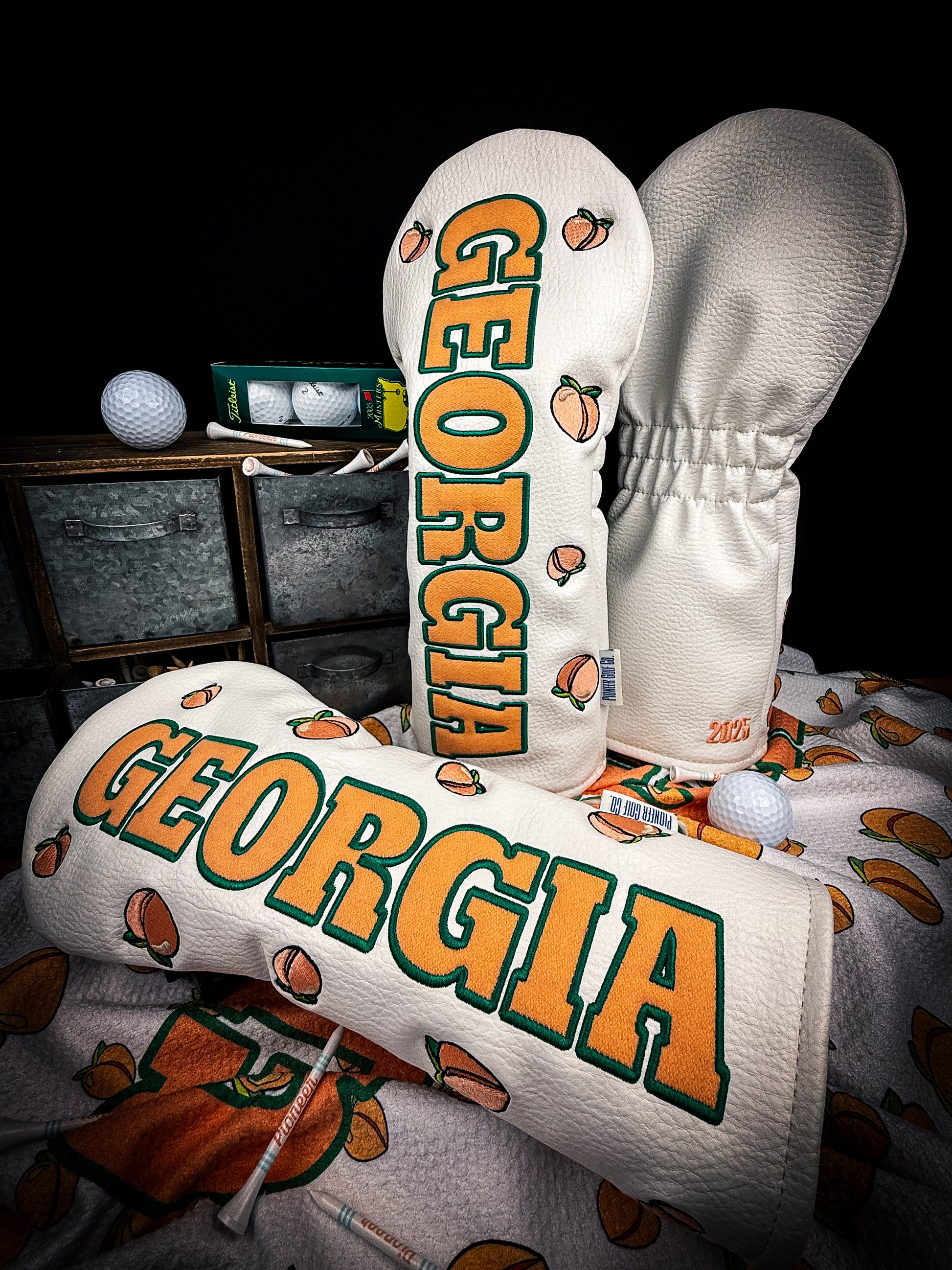 A golf club headcover featuring a pattern with the text 'Georgia' and images of peaches, displayed in a pro shop.