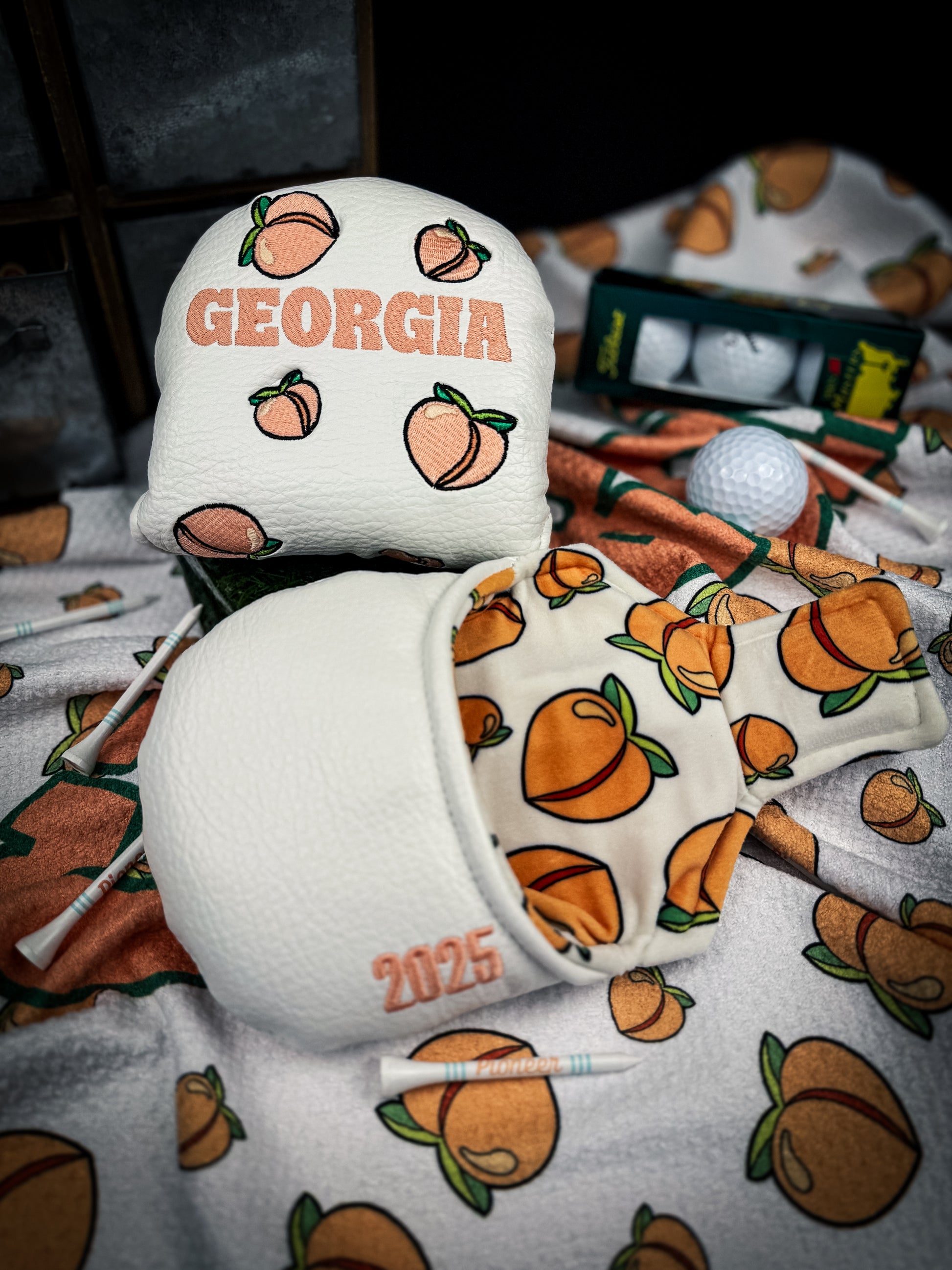 A golf club headcover featuring a pattern with the text 'Georgia' and images of peaches, displayed in a pro shop.